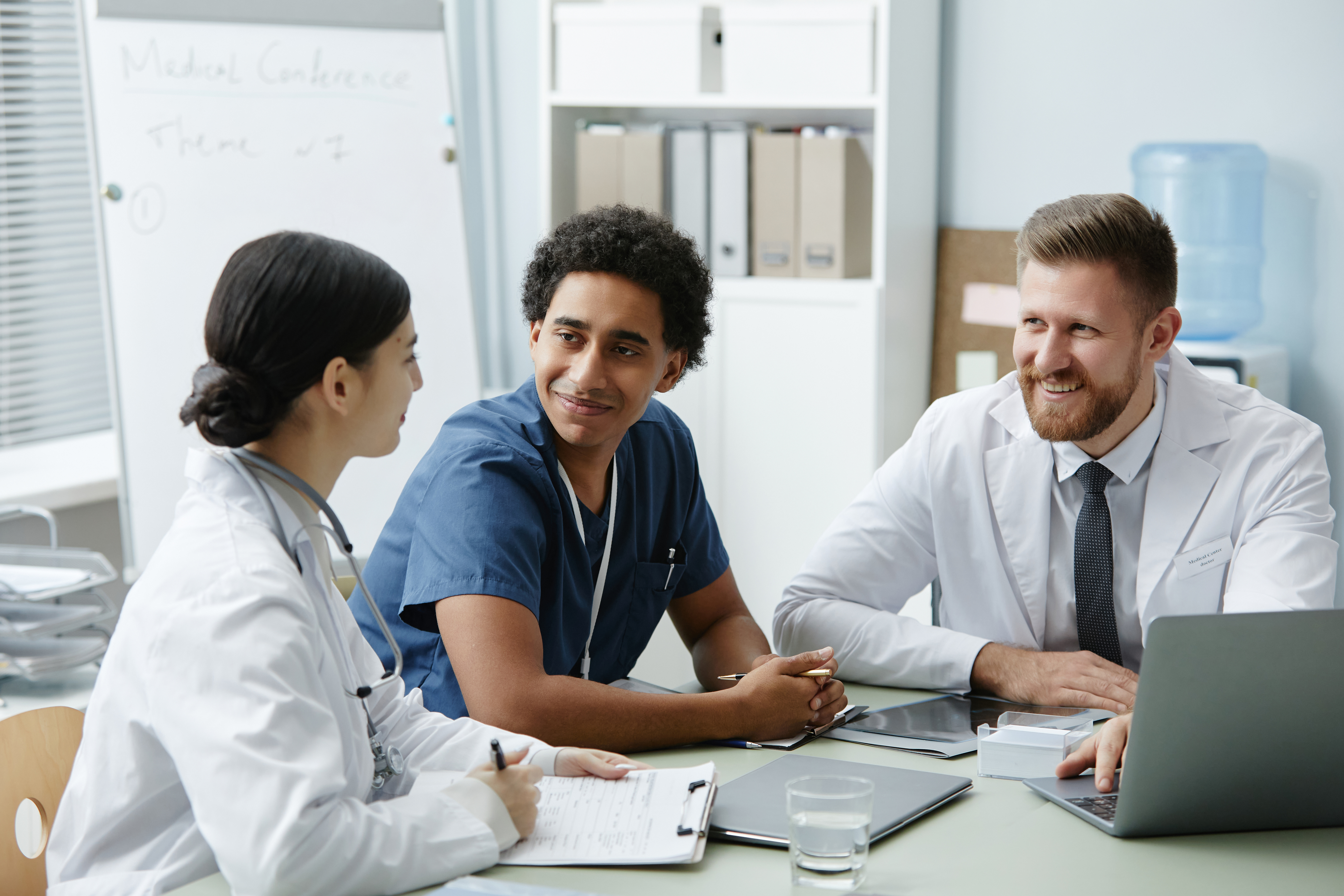 Group of Three Smiling Doctors Meeting at Table in Clinic