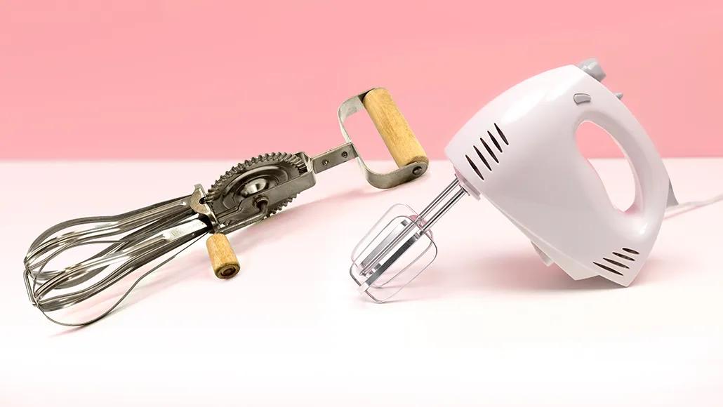 An old hand-crank egg beater next to an electric hand mixer.