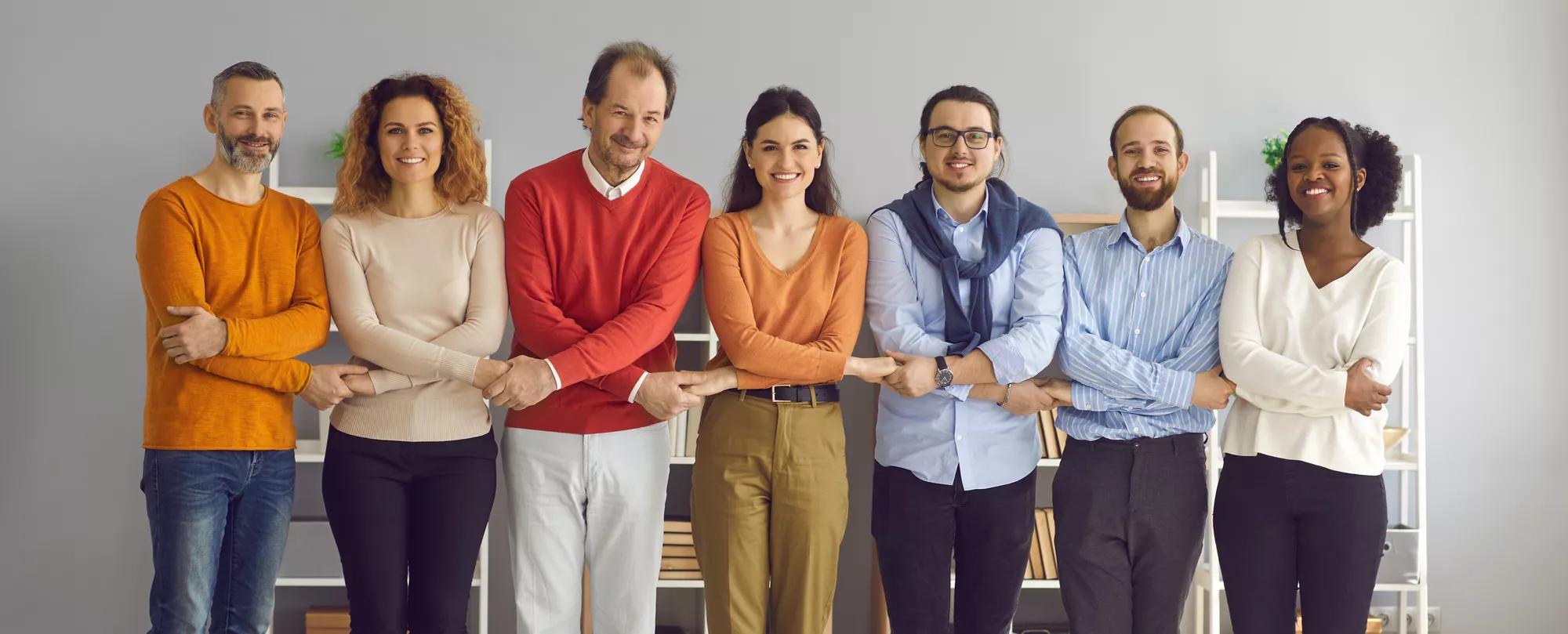 Group of happy diverse people showing their unity and support. Team of cheerful smiling multi generational colleagues, friends or community members of different ages standing in row and holding hands