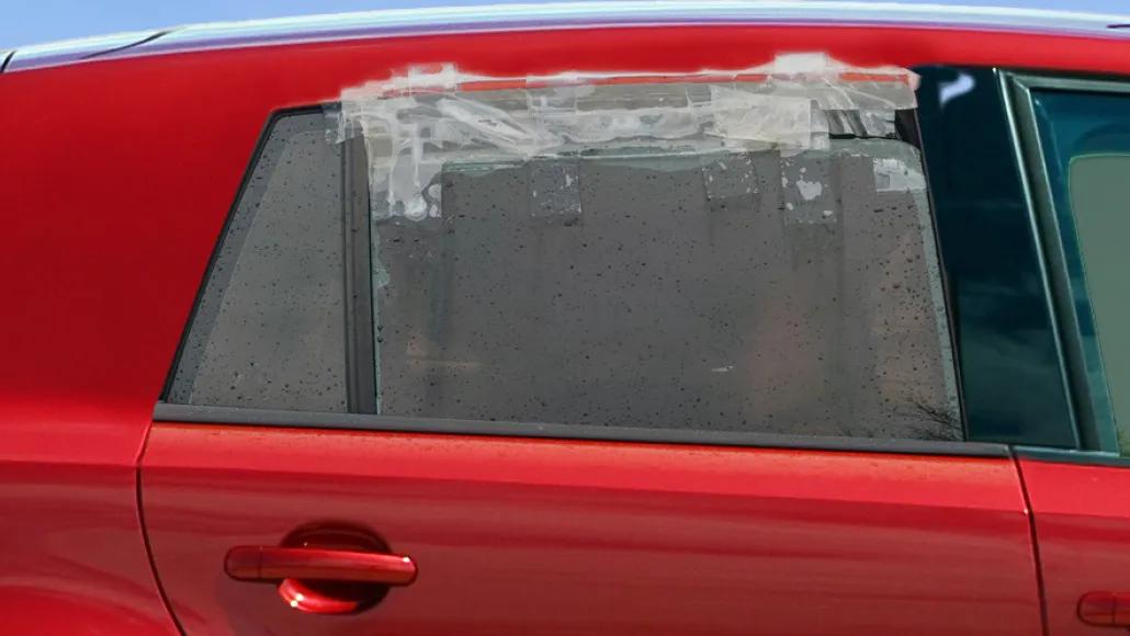 An image of the back passenger side of a red car with tape covering the gap of the slightly rolled down window