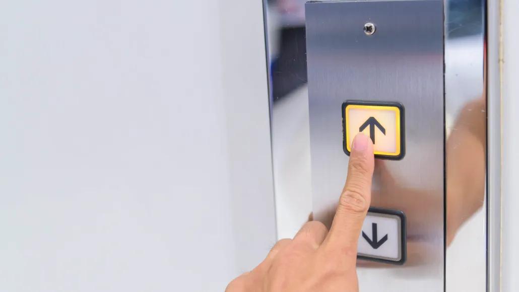 A photo shows a finger pressing the up arrow of an elevator button