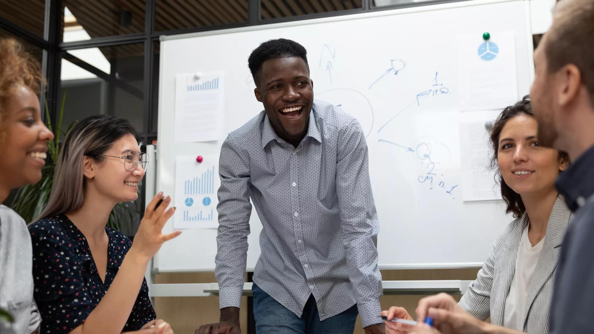 Excited African American leader holding briefing, listening to colleague sharing creative startup idea, diverse employees having fun at meeting close up, laughing at joke, staff good relations