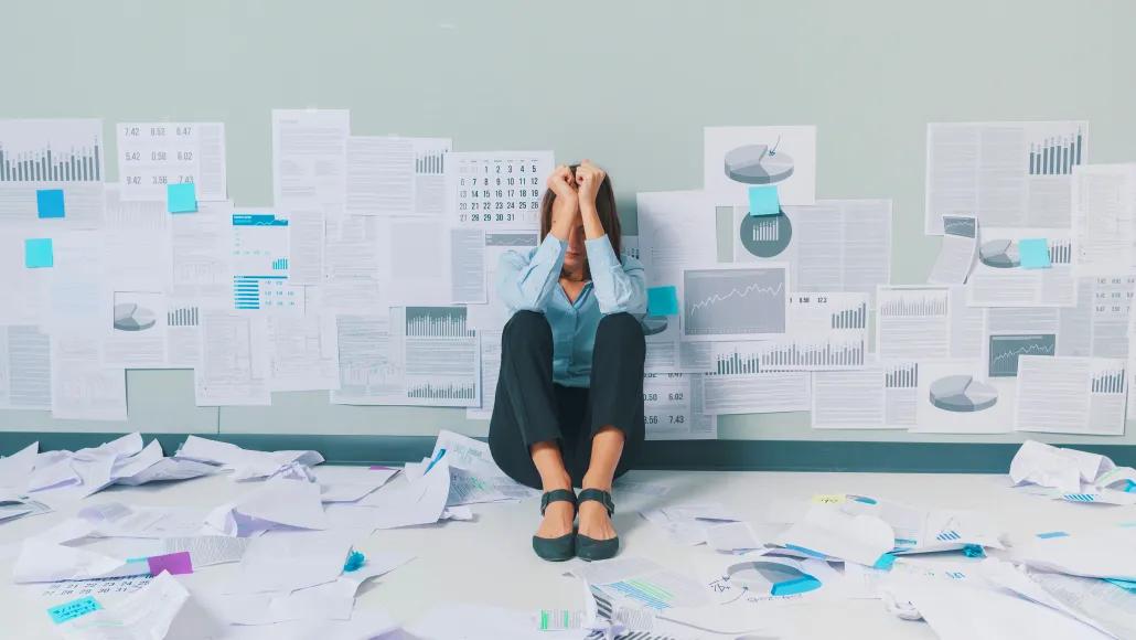 A photo shows a despondent worker surrounded by numerous data-related sheets of paper.