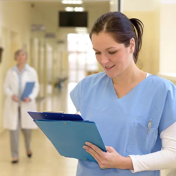 A female health care worker reviews a file in a hospital corridor.