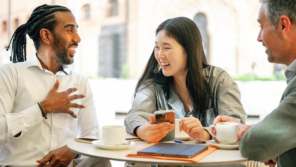 Three co-workers laugh and drink coffee at a café.