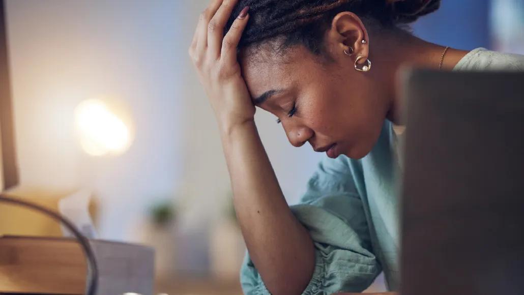 A woman sits at a desk and puts her palm to her forehead in despair.