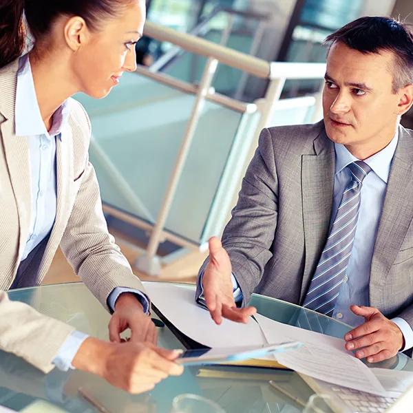 Two business colleagues sit together at a table in the office talking.