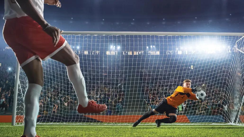 A photo shows a soccer goal keeper blocking a ball that was kicked toward the goal by another player.