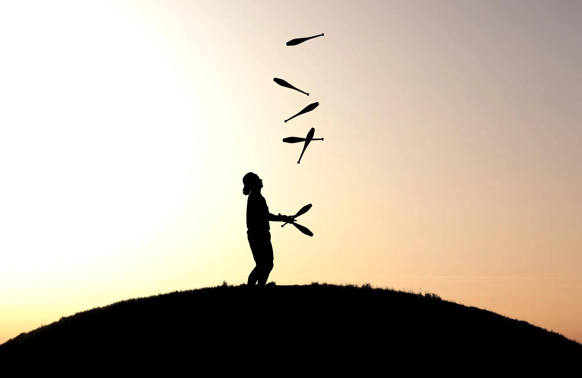 circus artist juggling with seven juggling clubs in sunset