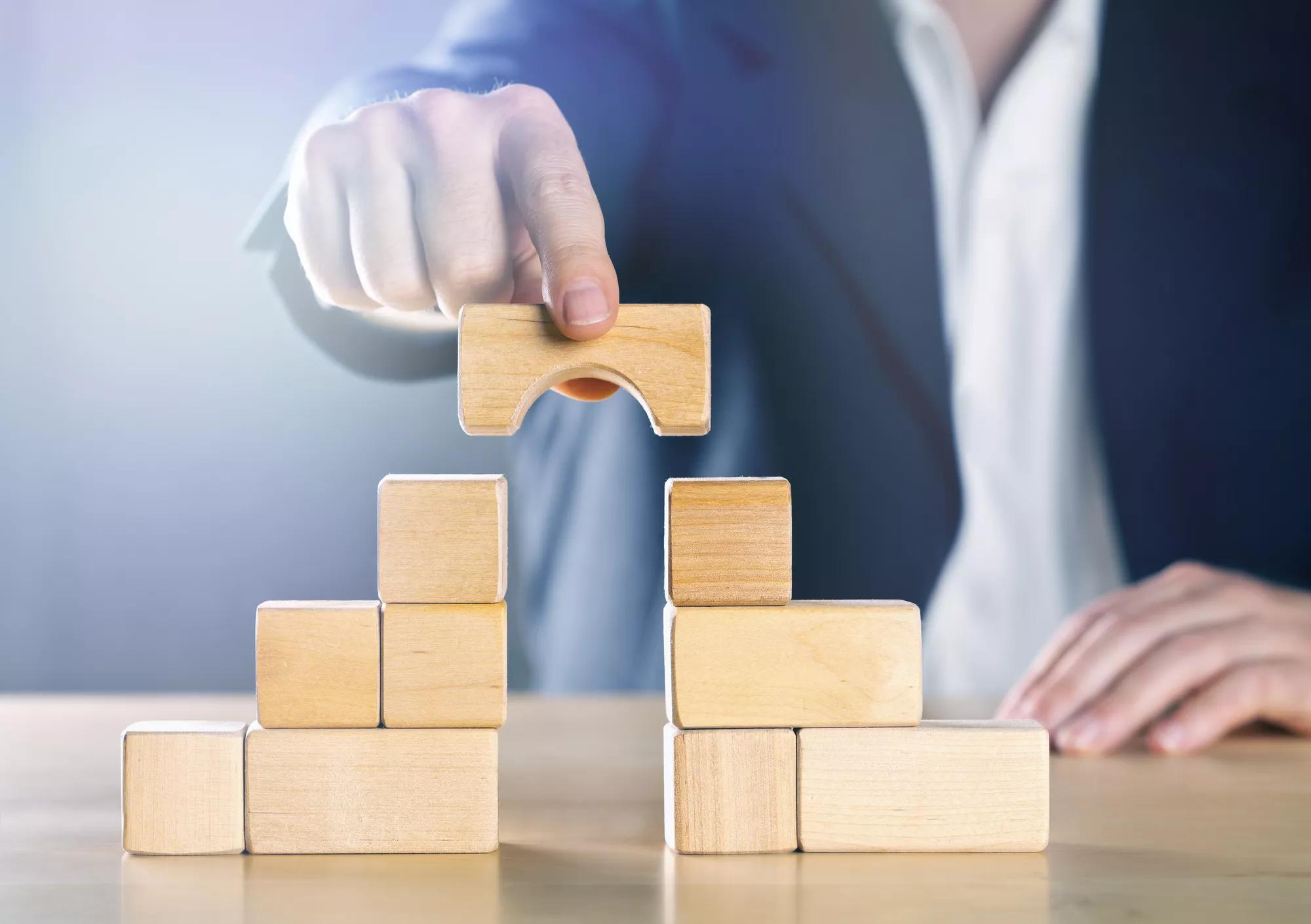 Business man bridging the gap between two towers or parties made from wooden blocks; conflict management or mediator concept