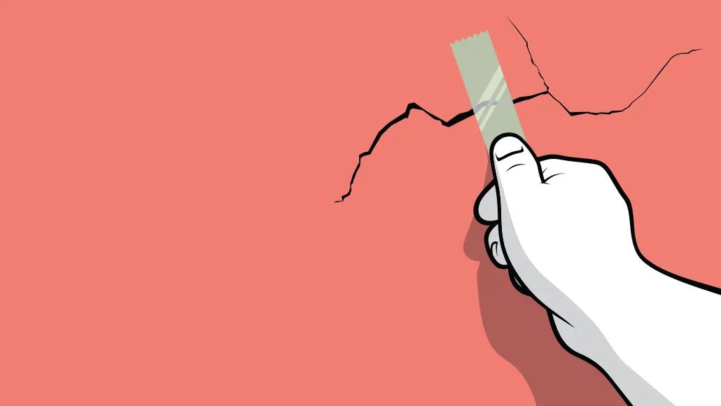 A hand places a piece of tape over a crack in a wall.